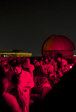 Crowd under red lighting at night, with dome in the background.