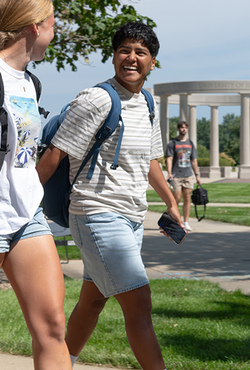 Students smiling, walking on grassy campus with backpacks.