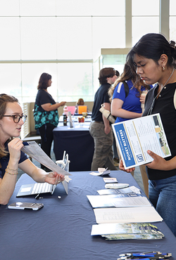 Woman at table discussing brochures with an attendee at an event.