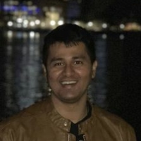 Sriram Krishnan standing in front of a river at night with tall city buildings behind him
