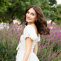 Smiling woman in a white dress stands in a lavender field.
