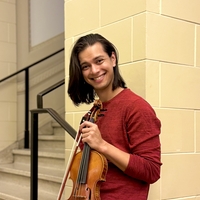 Smiling person holding a violin by a stairwell.