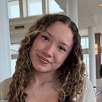 Smiling person with curly hair in a bright room.
