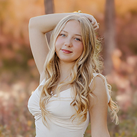 Young woman with long hair poses in a sunny, blurred autumn setting.
