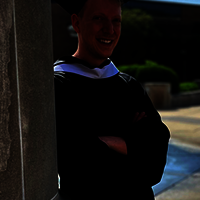 Graduate in cap and gown standing by a column.