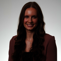 Smiling woman with long brown hair, wearing a maroon blazer.