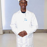 Man in a white coat and helmet standing indoors.