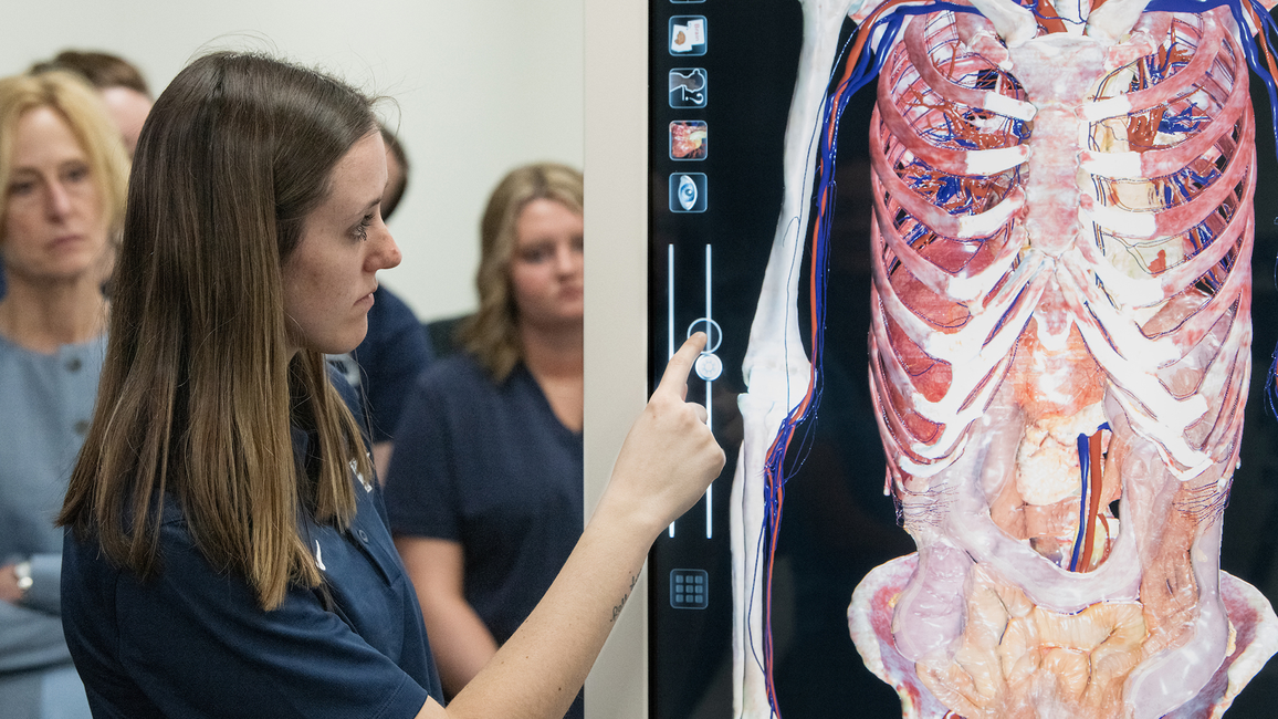 A student stands next to an antomage table, adjusting its functions on the screen.