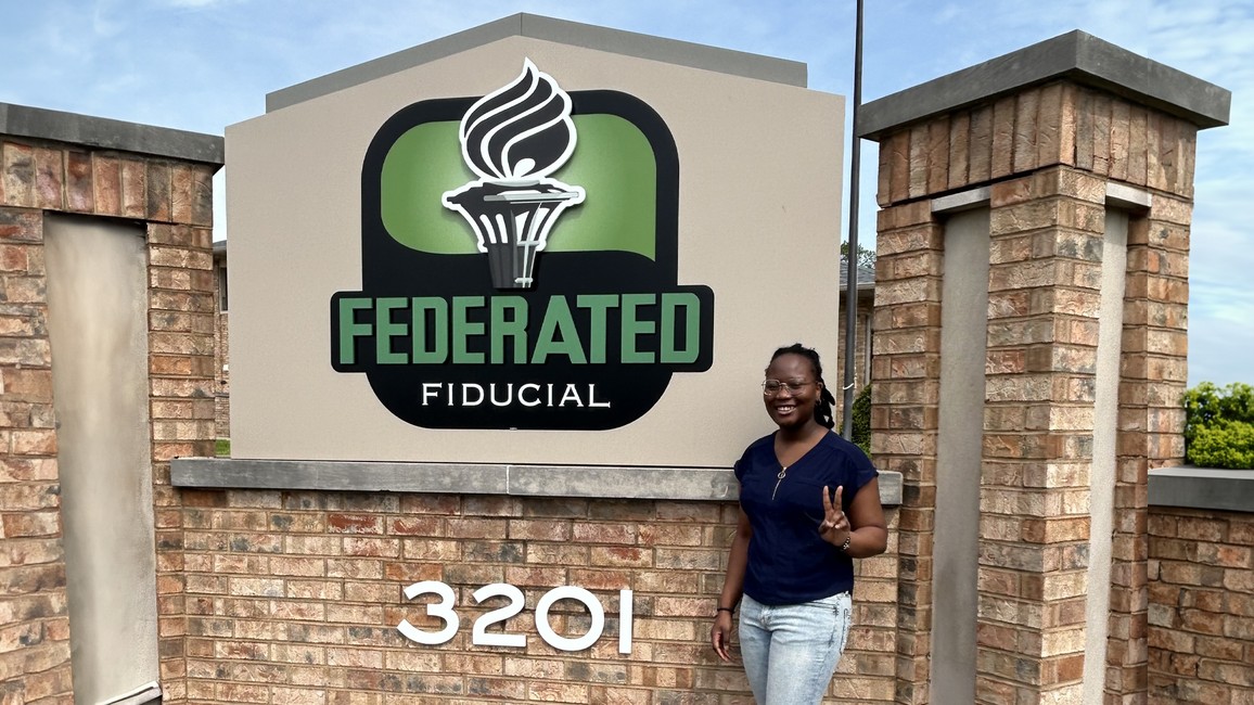 UIS student Wonder Odutola stands next to Federated Fiducial sign.