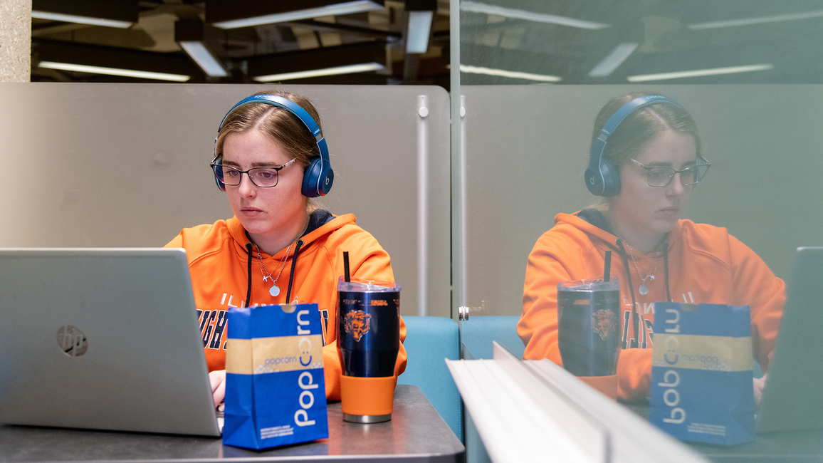 A student wearing headphones uses a laptop computer to study in Brookens Library.