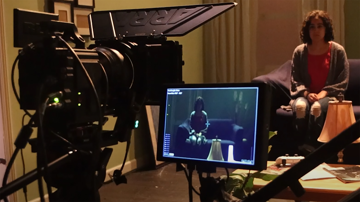 A camera and screen and shown capturing an image of a girl sitting on a couch.