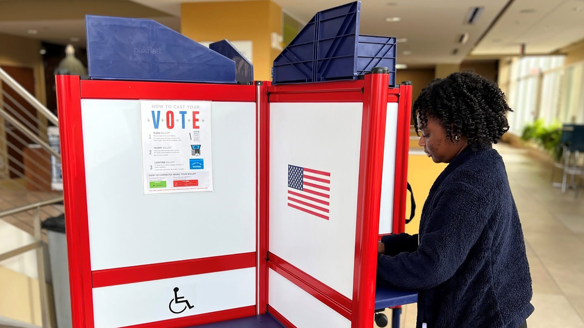 Student casts ballot at a red, white and blue voting booth inside the University of Illinois Springfield student union.