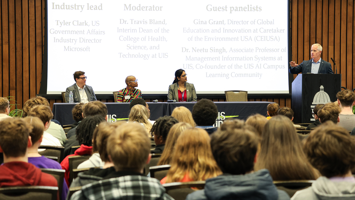 Panelists speak to a large audience at a UIS AI-themed event with a presentation screen in the background.