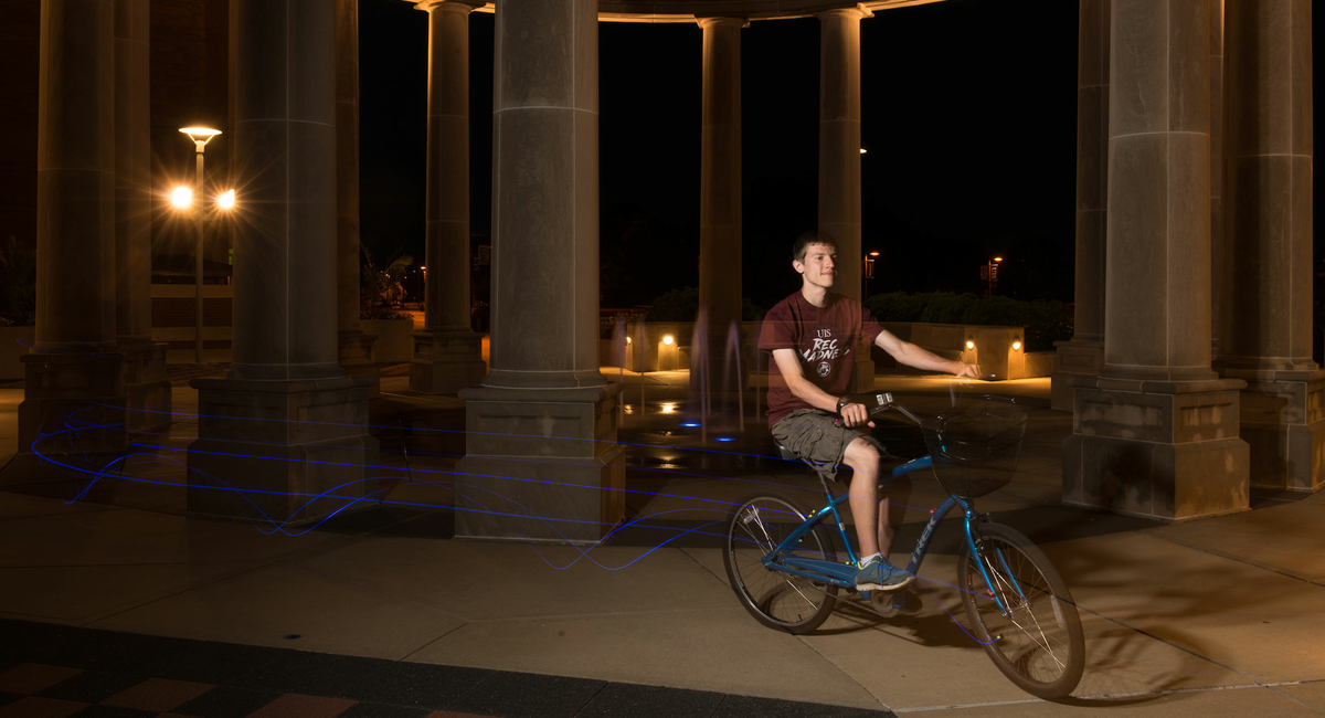 a male student riding his bike through the colonnade at night