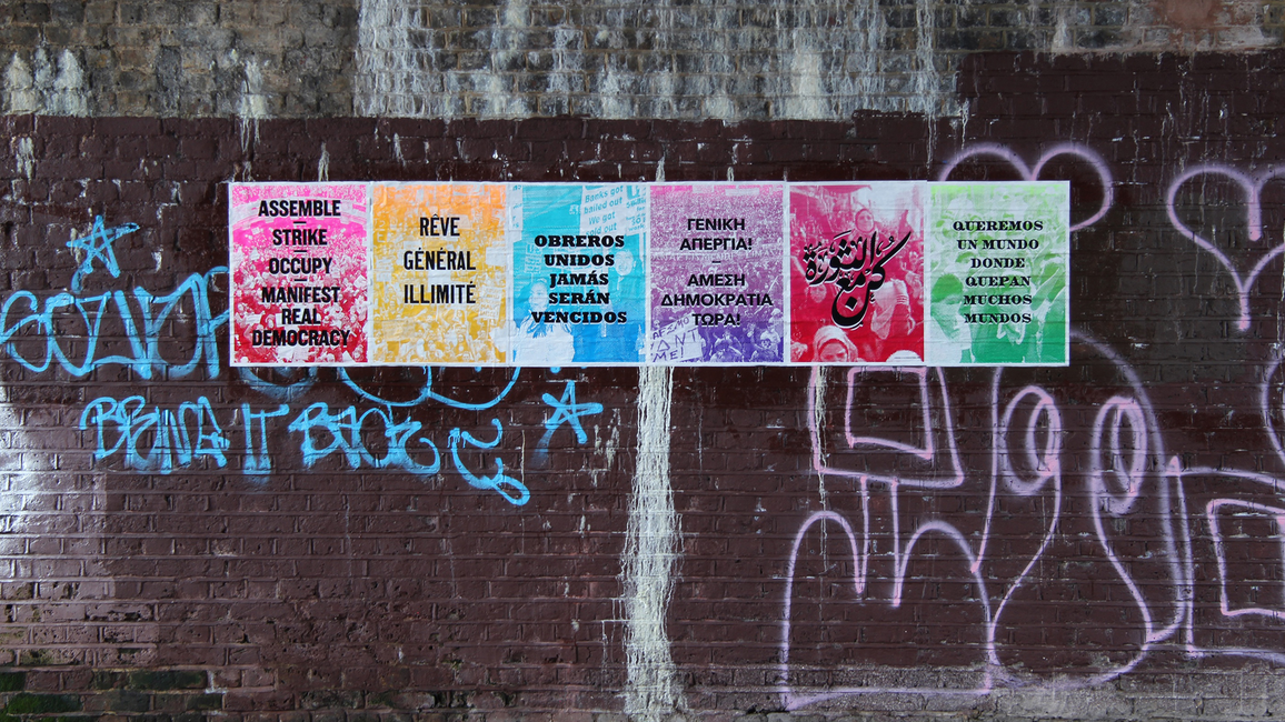 A vibrant poster series on a graffiti-covered brick wall. Each colorful panel displays multilingual text.