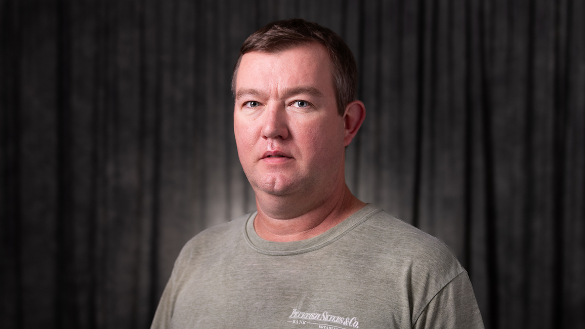 Cory Strawn, a man in a grey shirt with a neutral expression, dark background.