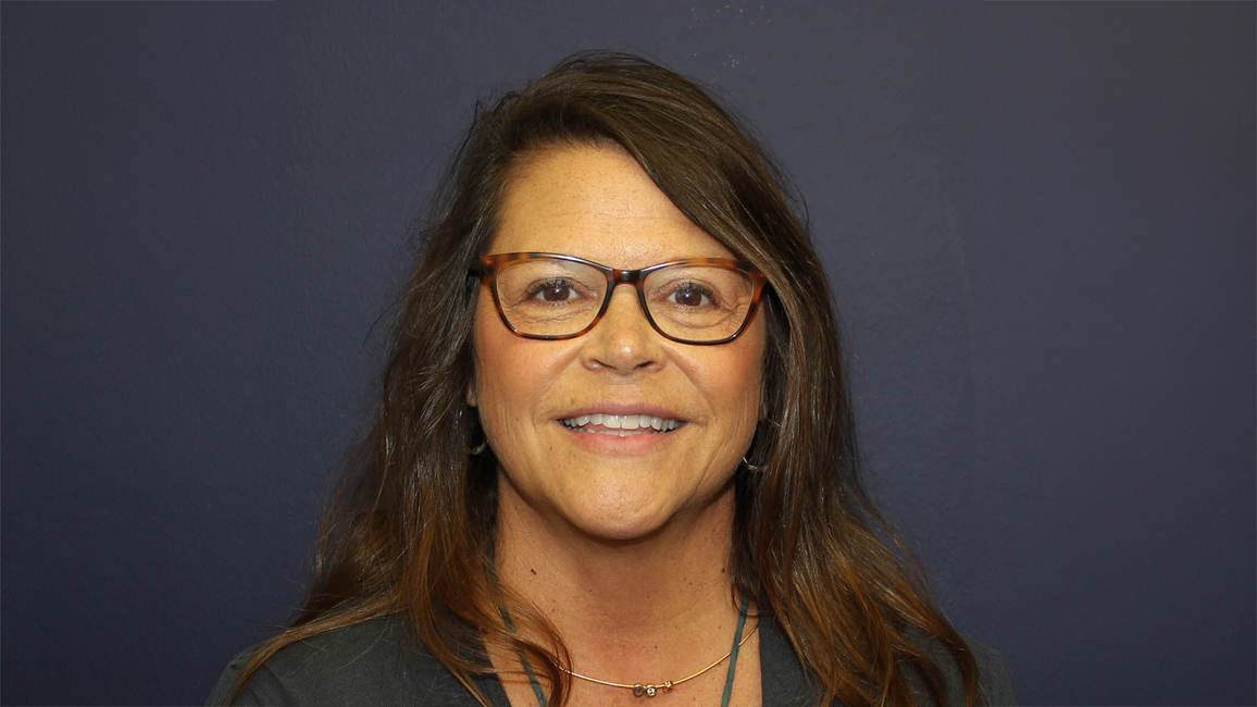 Smiling woman with glasses against a dark background.