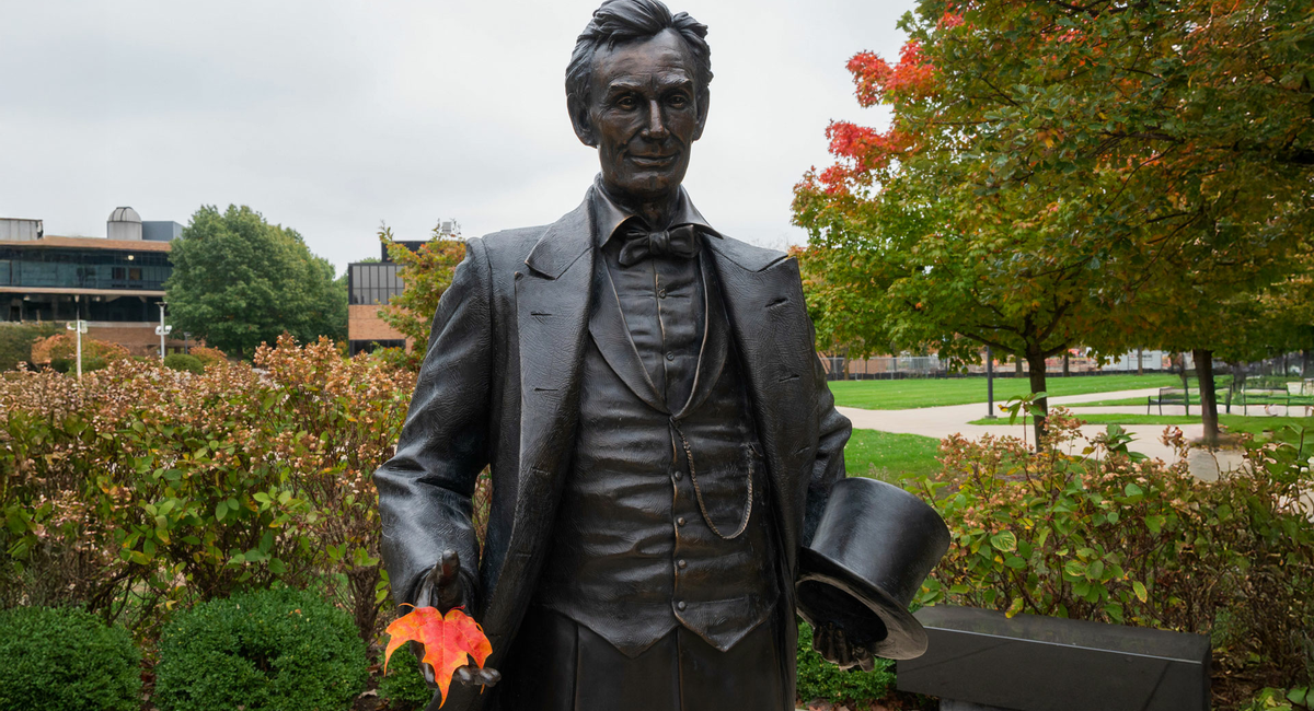the lincoln statue on campus holding an orange autumn leaf in his hand