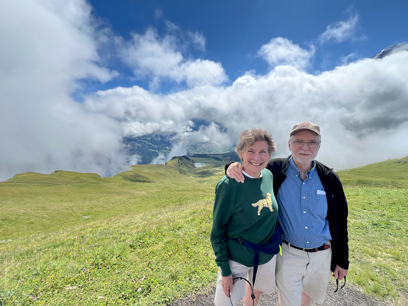 President Tim Killeen and wife, Roberta, standing on a grassy hill under a cloudy sky, smiling at the camera.