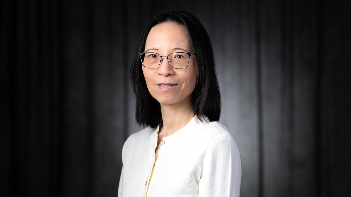 Woman with glasses, wearing a white top against a dark backdrop.