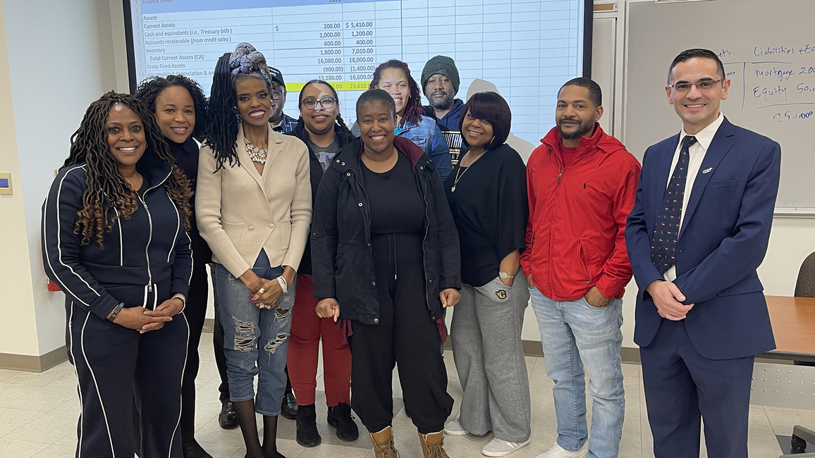Group of people standing in a classroom, smiling at the camera.