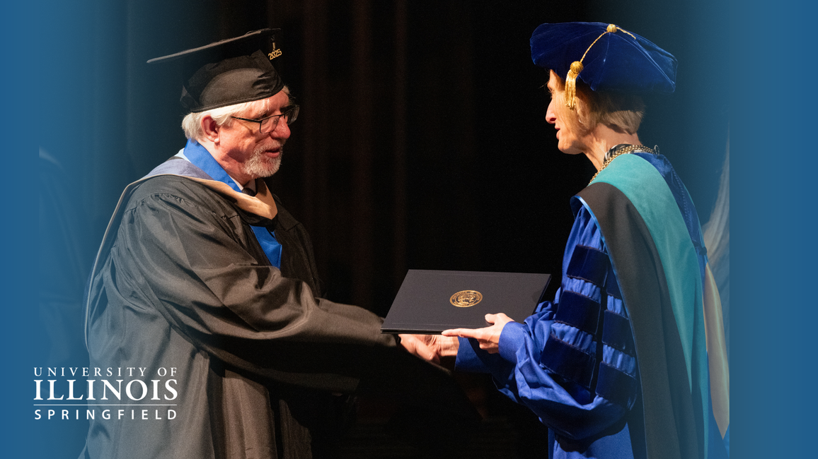 A graduate receives a diploma from a faculty member in academic regalia.