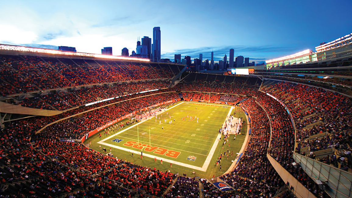 Wide-angle view of a football stadium at dusk, city skyline in the background.