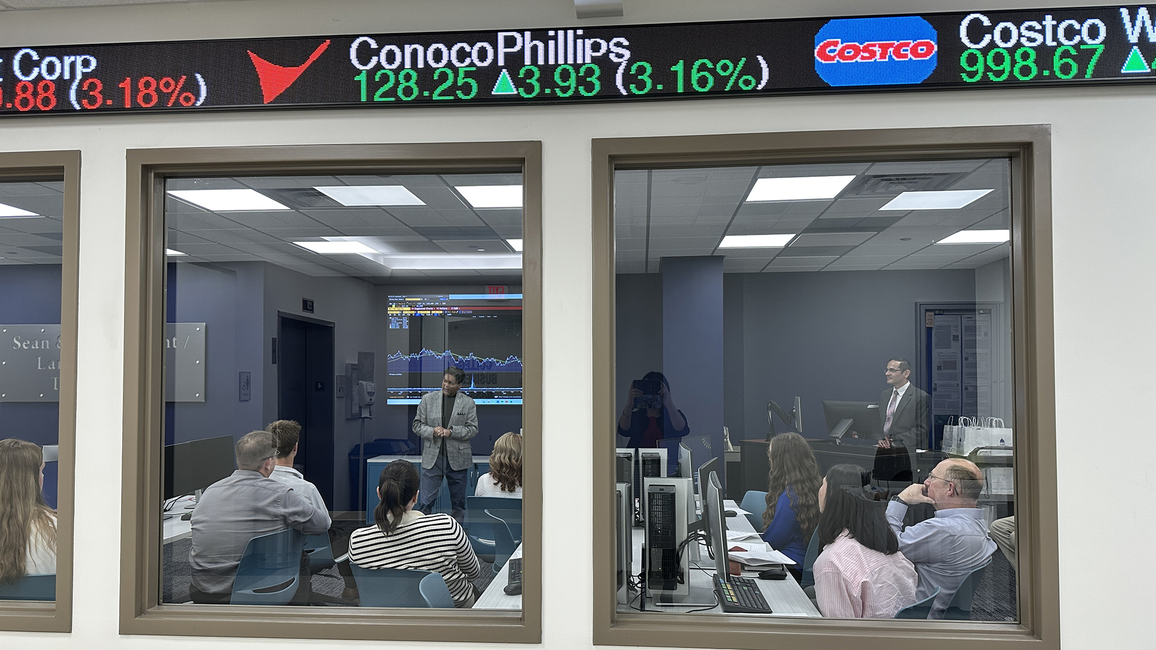 Office meeting seen through a window, stock ticker overhead.