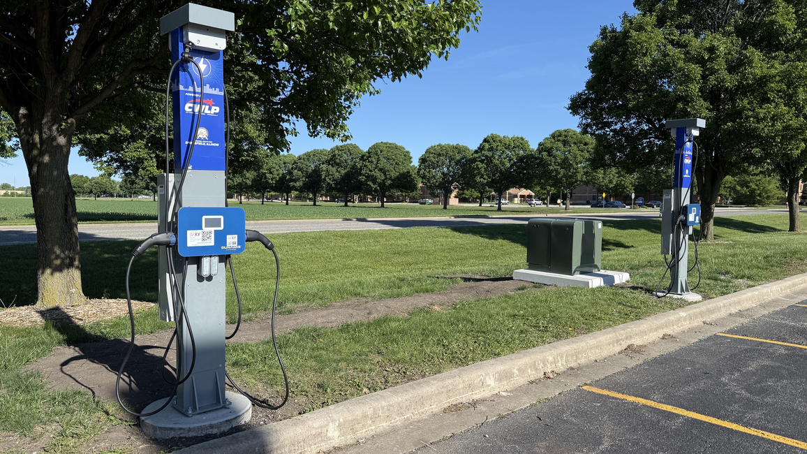 Electric car charging stations in a park with trees and a clear blue sky.