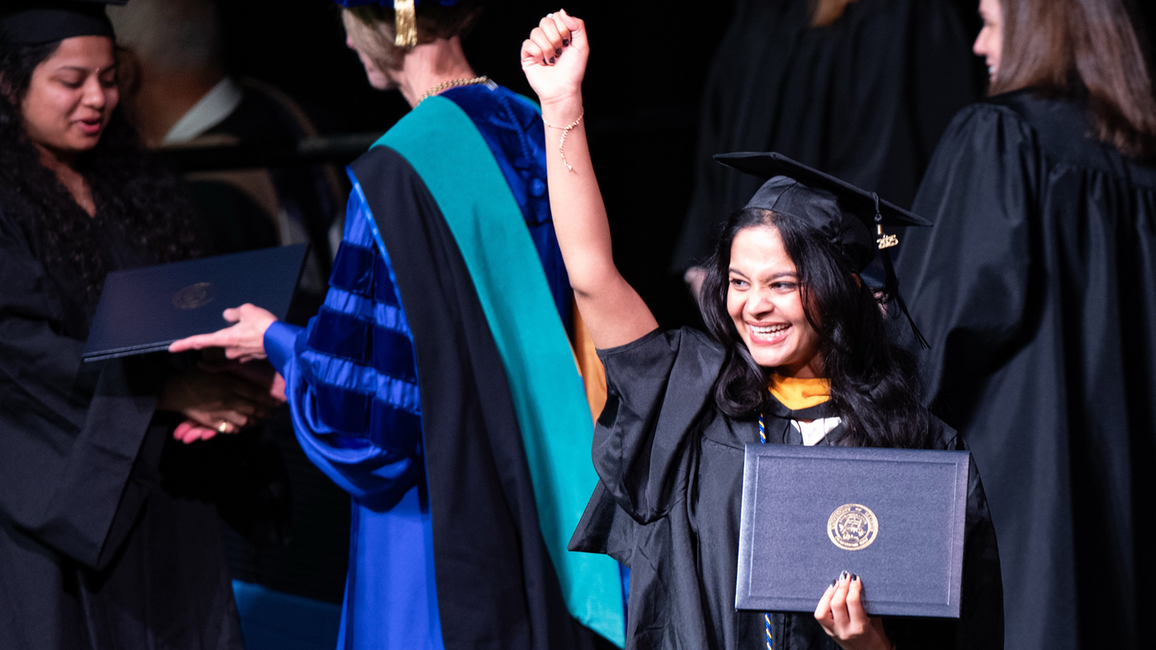 Graduate proudly holding diploma, smiling, surrounded by people in academic gowns.