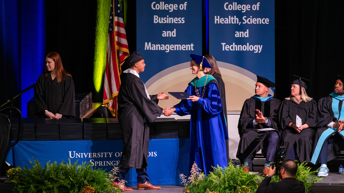 Graduate shaking hands with official on stage at graduation ceremony.