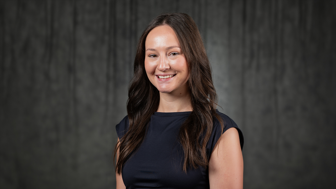 Smiling woman in a black dress against a dark backdrop.