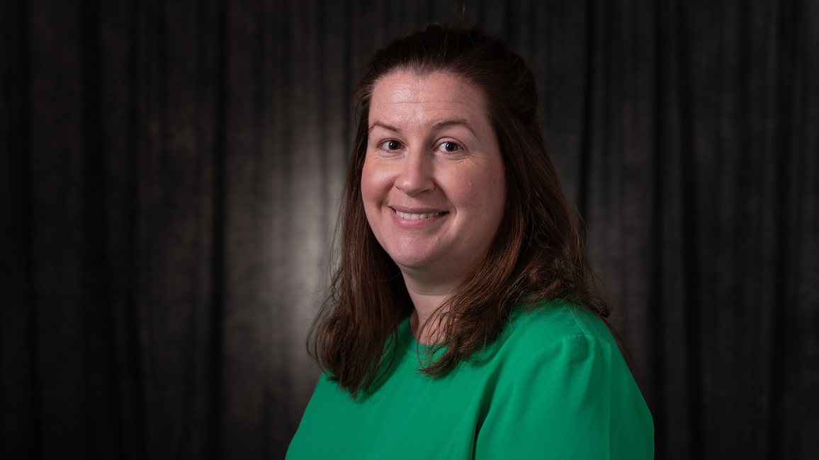 Smiling woman in a green top against a dark background.