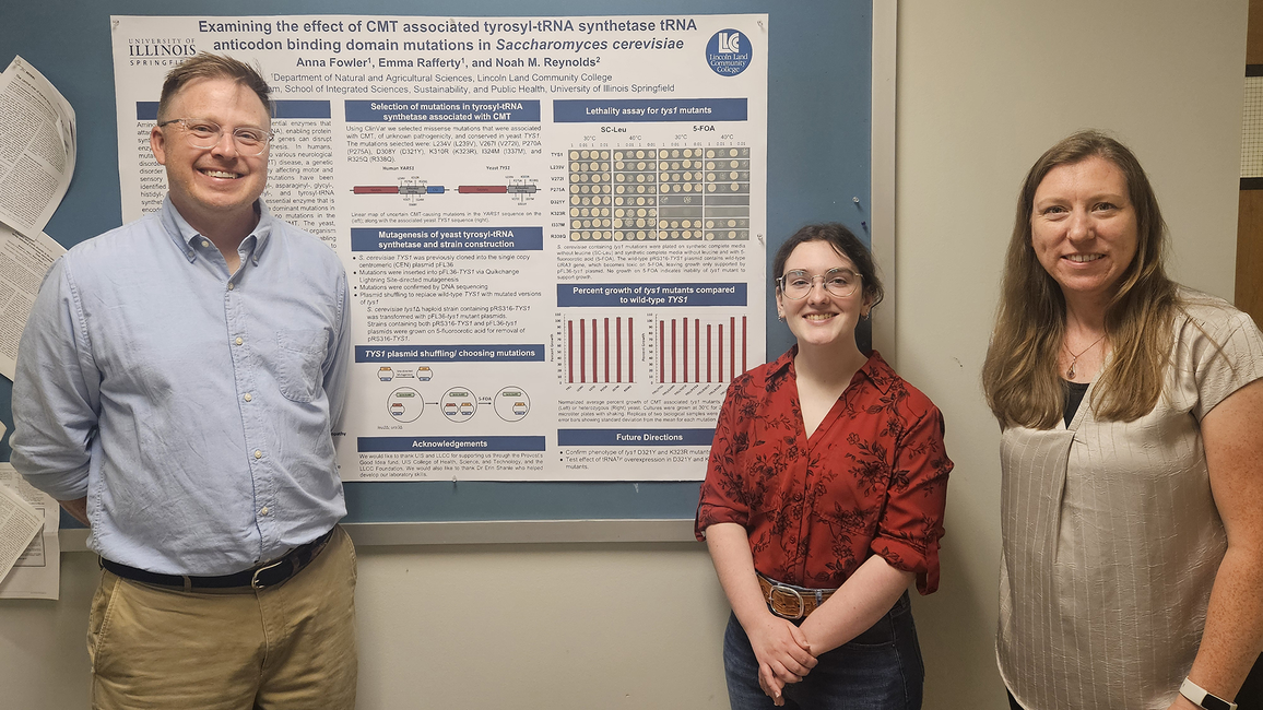 Three people smiling in front of a research poster display.