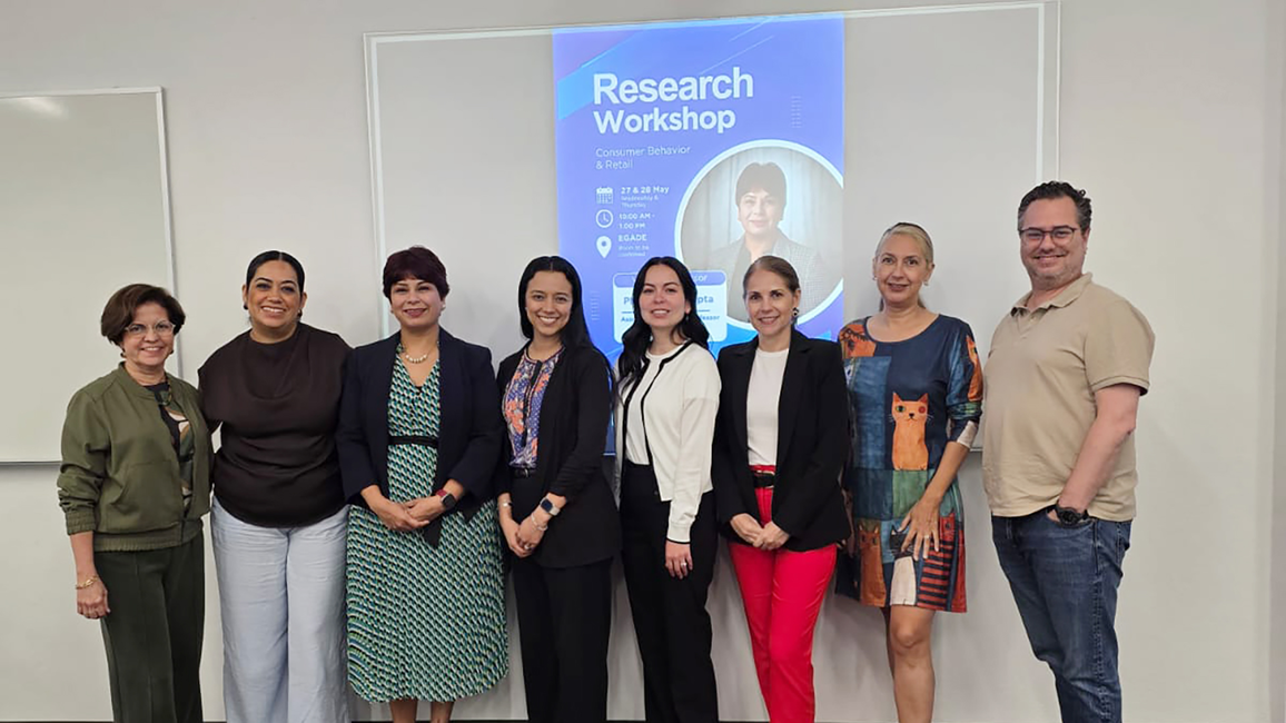 Group of eight people smiling in front of a research workshop poster.