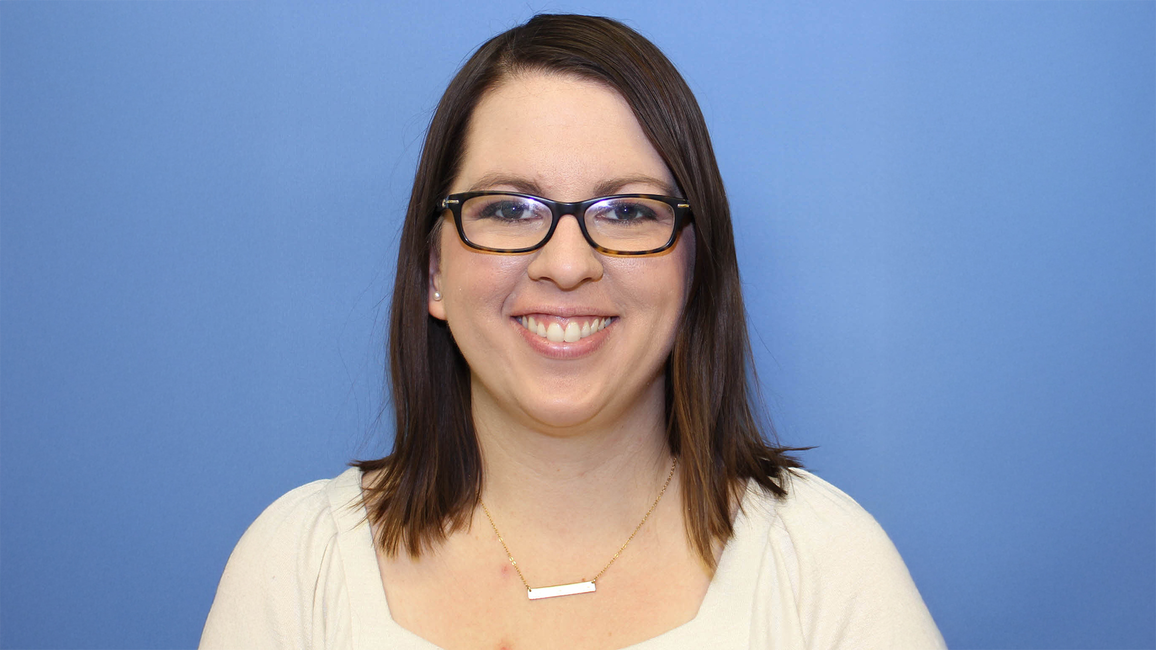 Smiling woman with glasses, wearing a white shirt against a blue background.