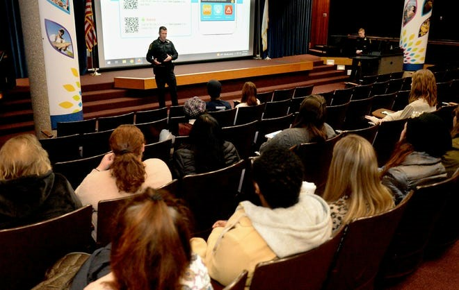 Audience listens to a presentation from police officers in an auditorium setting.