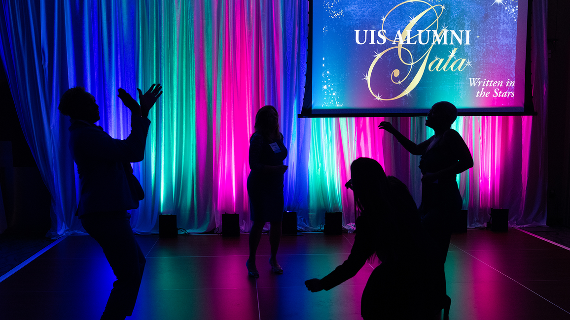 Silhouettes dancing against colorful lights at an event.