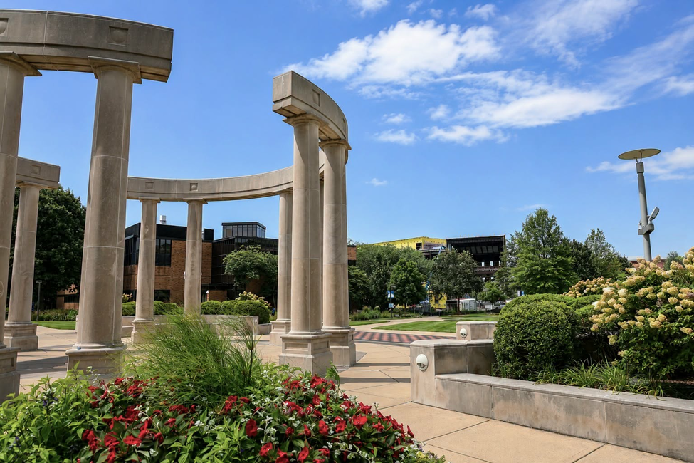 Stone columns in a sunny garden with blue sky and clouds.
