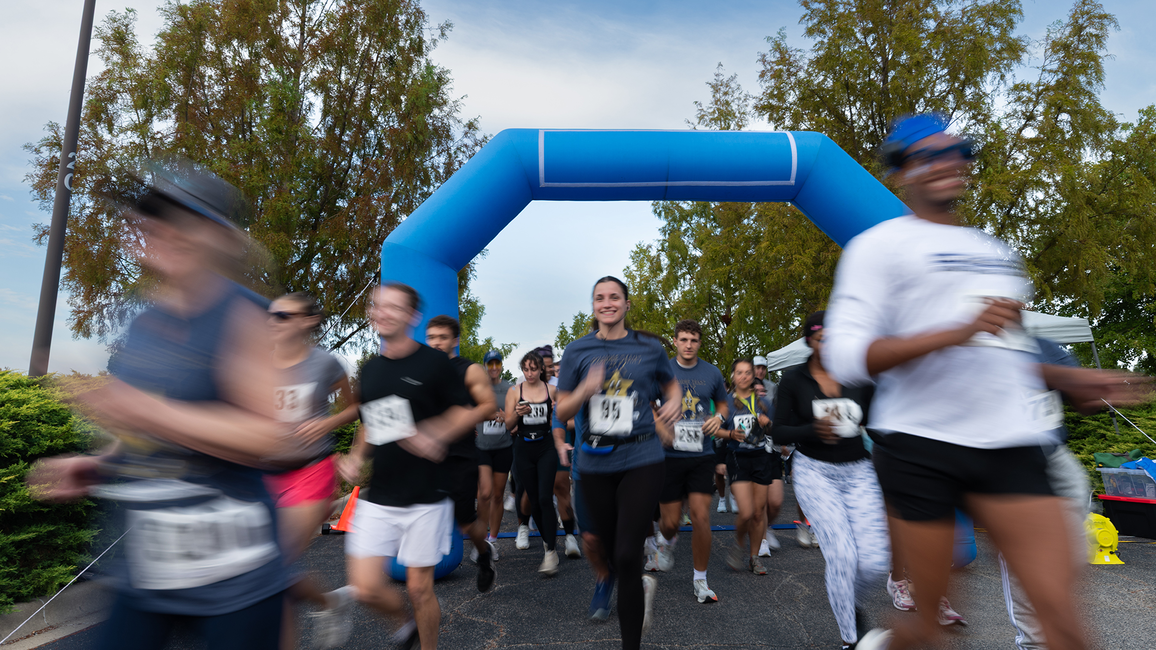 Runners in a race, under a blue inflatable arch, with blurred motion.