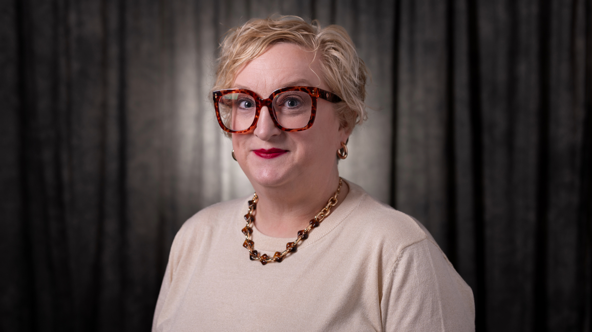 Sarah Adams smiling at the camera with a grey background.