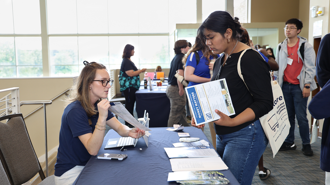 Student receives brochures at a college fair booth.