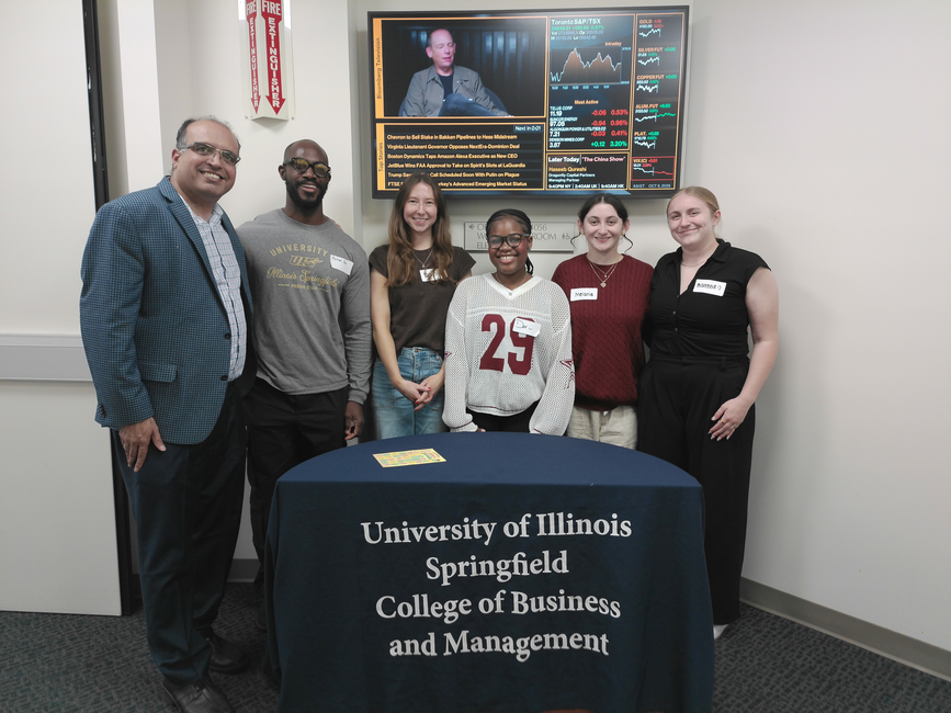 Six UIS students and faculty member pose behind a University of Illinois Springfield College of Business and Management table during an event.