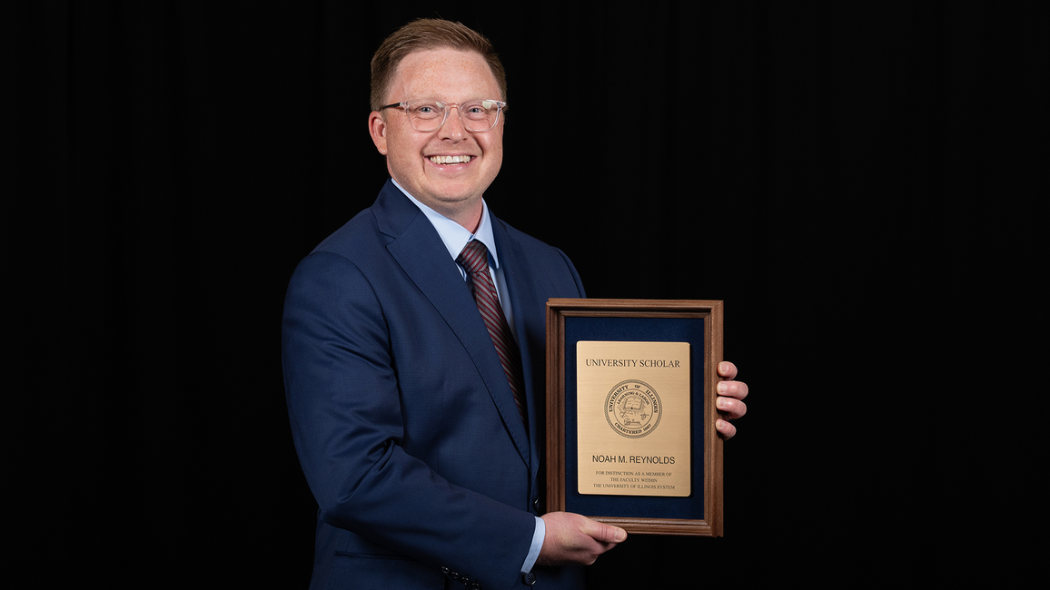 Man in a suit smiling, holding a plaque against a black background.