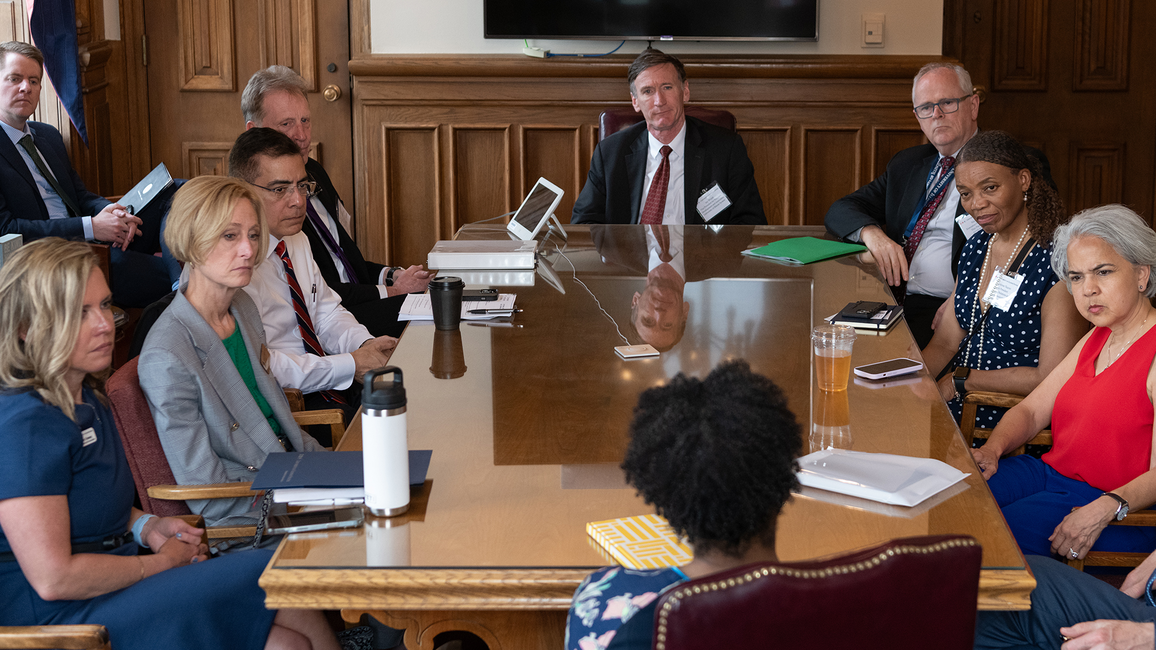 Meeting in a boardroom with people seated around a wooden table.