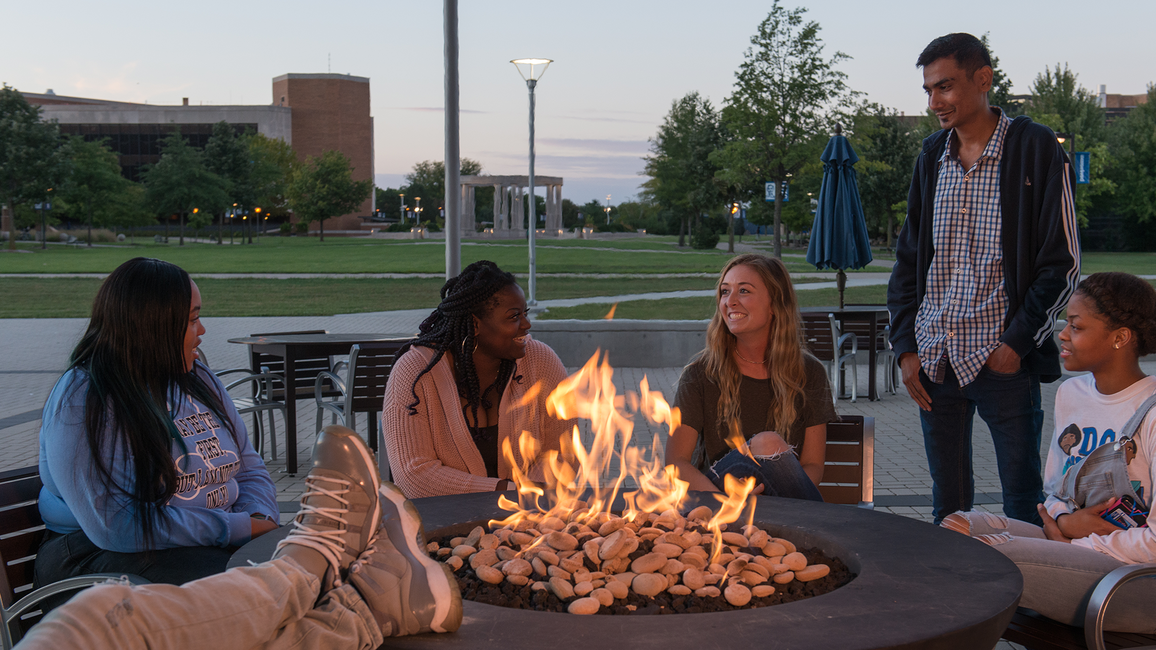 People gathered around a fire pit at dusk, smiling and talking.