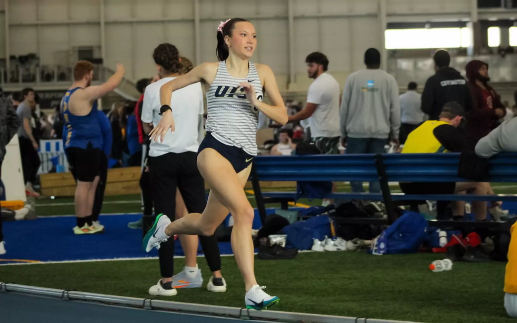 Madelyn Miller-Ross running indoor track in white UIS uniform