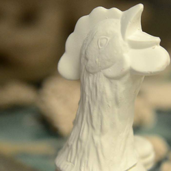 Ceramic rooster head with other ceramic works in the background.