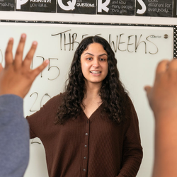 a teacher in the middle of a classroom with lots of raised hands