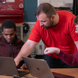 a professor explaining something on a computer to two students